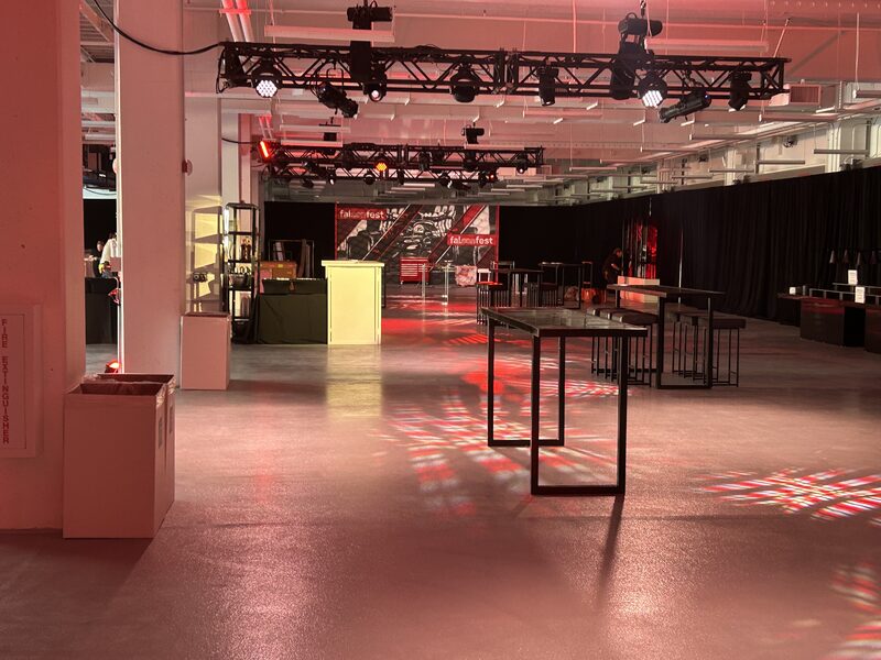 Event venue with a truss lighting rig, stage equipment, and red accent lights during setup
