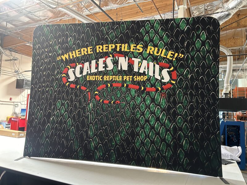 Scale and Tails event backdrop with reptile-scale graphics and a colorful headline