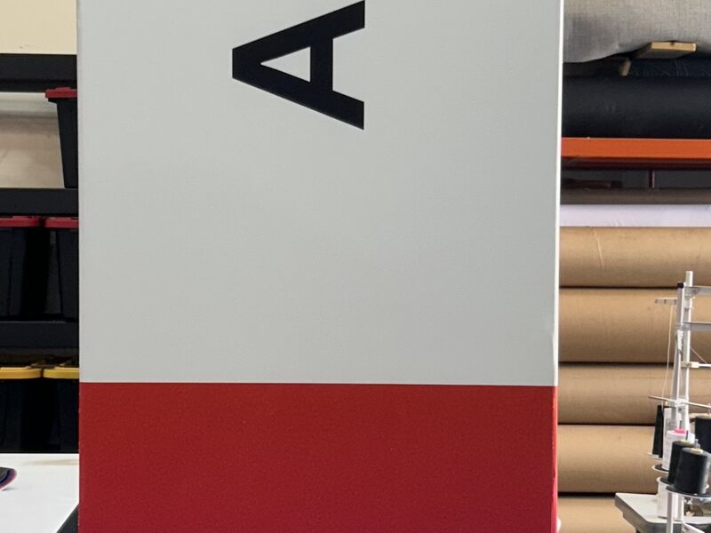 Tall exhibit wayfinding column with large black lettering and a red base