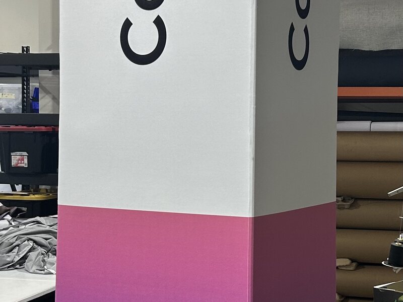 Tall exhibit wayfinding column with large black lettering and a magenta base