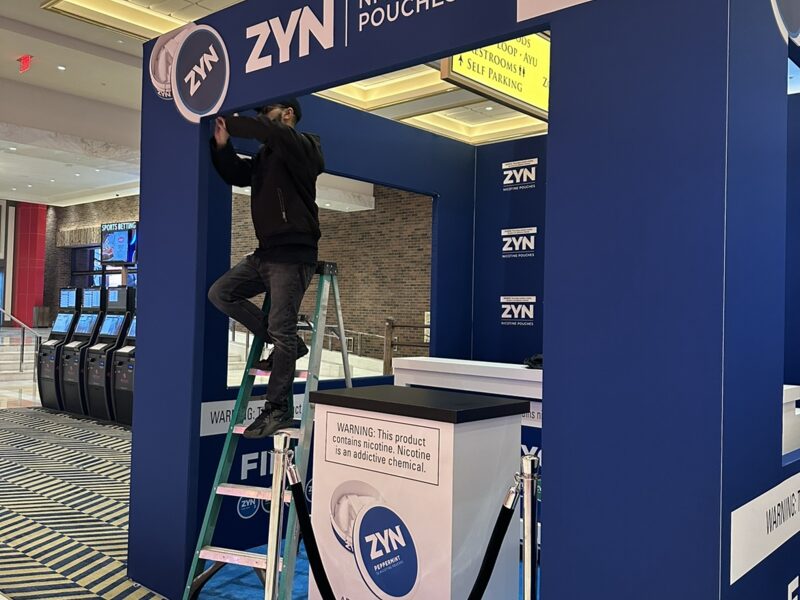 Worker on a ladder fitting graphics to a blue ZYN promotional display