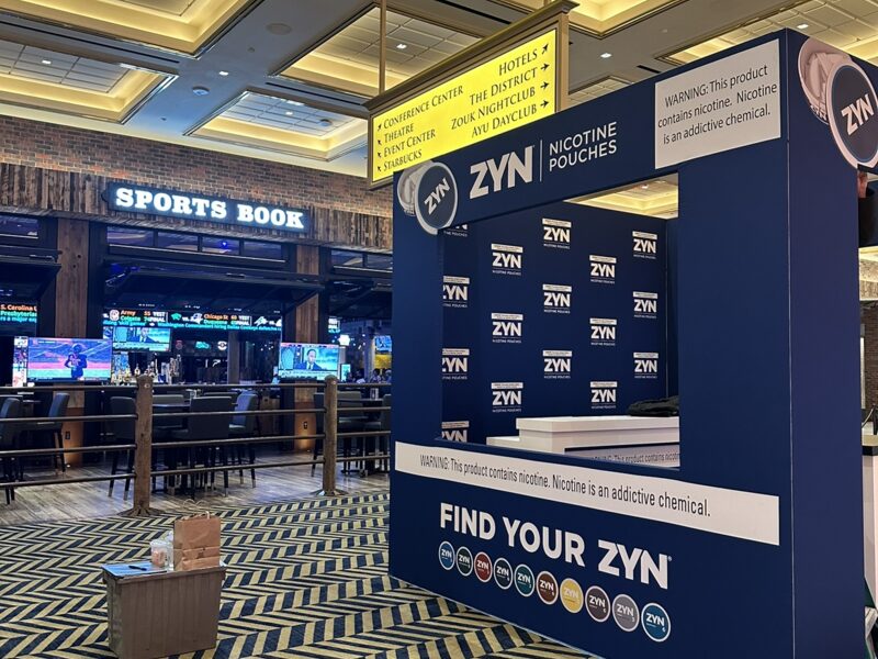 Blue ZYN branded display beside a sports book, shown from the aisle